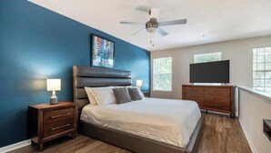 Un dormitorio con cama, mesitas de noche, televisor y ventilador de techo.