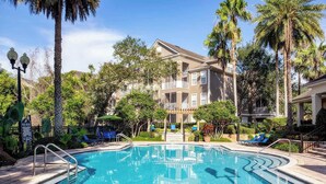 A pool area with a clear blue pool, lounge chairs, and palm trees. - Landing | Modern 1BD, Gym, Pool (Orlando)