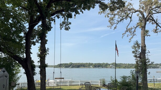 A lakeside patio with a table and chairs, a swing set, and an American flag.