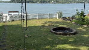 A backyard with a swing set, a fire pit, and a view of a lake.