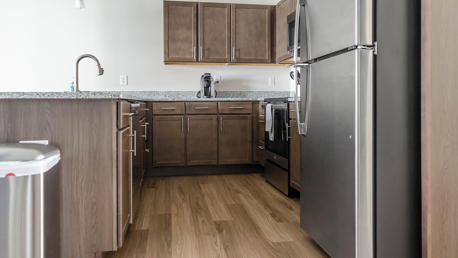 A compact kitchen with wooden cabinets, a stainless steel refrigerator, and a granite countertop.