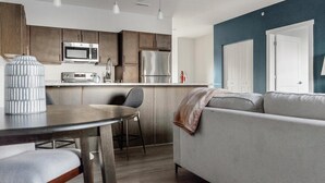 Una cucina moderna con elettrodomestici in acciaio inossidabile, una zona pranzo con tavolo e sedie, e un divano grigio davanti a una parete blu.