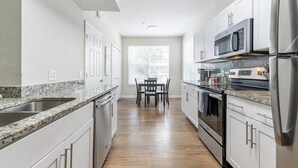 A modern kitchen with white cabinets, granite countertops, stainless steel appliances, and a dining area with a table and chairs. - Landing | Chic 1BD, Pool, Gym (Orlando)