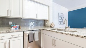 A modern kitchen with white cabinets, granite countertops, and a blue accent wall. - Landing | Stylish 2BD, Gym, Pool (Orlando)