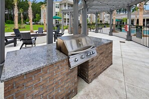 Un espace barbecue extérieur doté d’un plan de travail en briques et en pierres, entouré de chaises et d’un coin salon abrité.