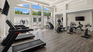 Ein großzügiges Fitnessstudio mit verschiedenen Cardiogeräten, großen Fenstern und einem Flachbildfernseher.