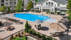 Ein großer Pool im Freien, umgeben von Liegestühlen, Sonnenschirmen und einem angelegten Garten.