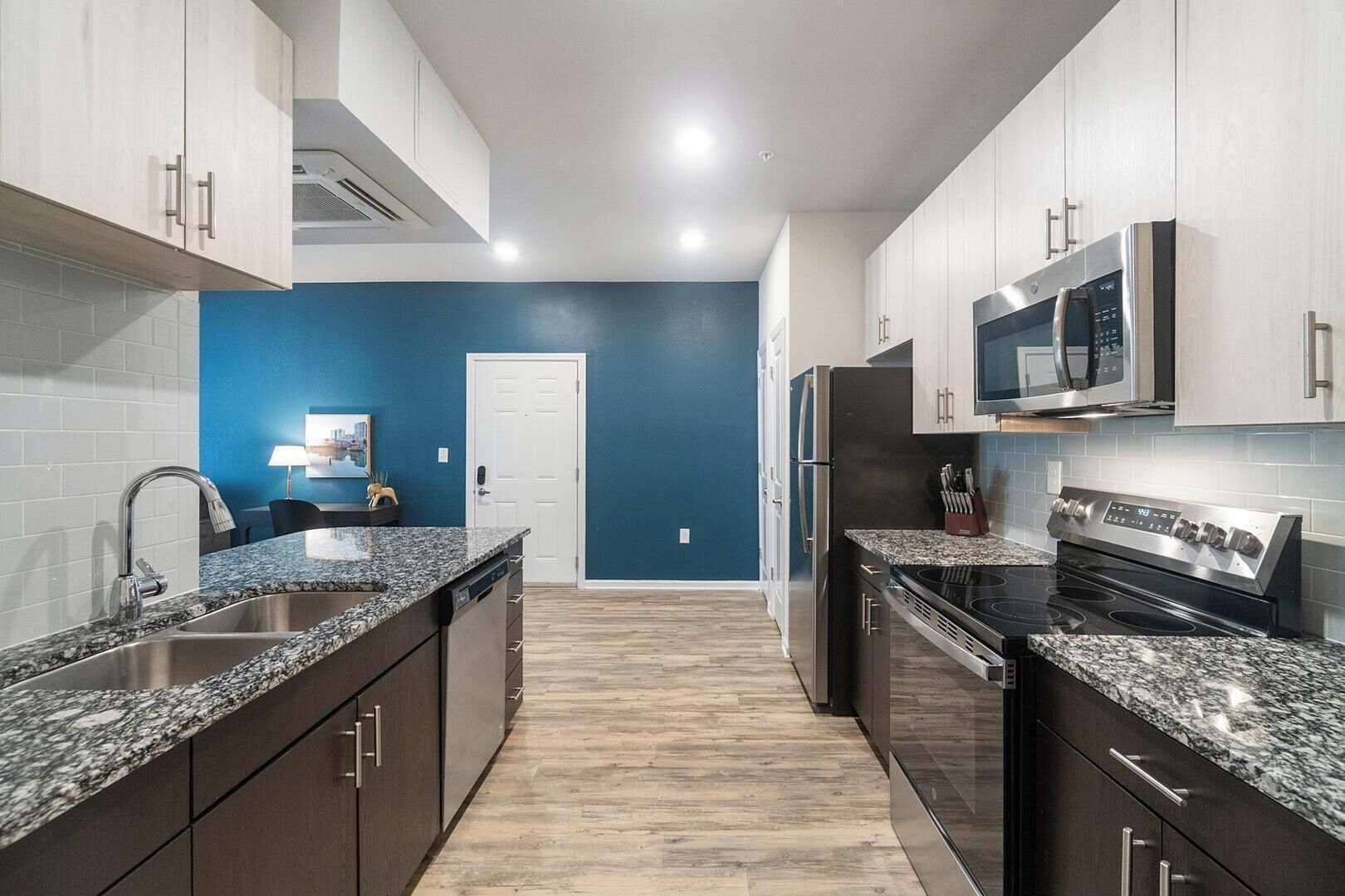 A modern kitchen with dark cabinets, granite countertops, stainless steel appliances, and a blue accent wall.