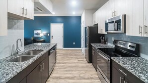 A modern kitchen with granite countertops, stainless steel appliances, and a blue accent wall. - Landing | Stunning 1BD, Gym, Clubhouse (Charlotte)