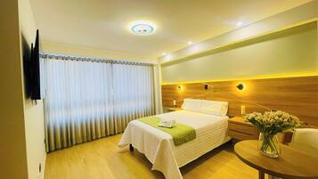Quarto de hotel com cama, mesa de cabeceira, abajur e uma pequena mesa com um vaso de flores.