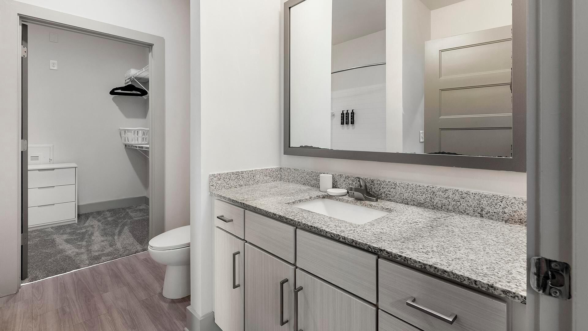 A modern bathroom with a granite countertop sink, a large mirror, and a walk-in shower.