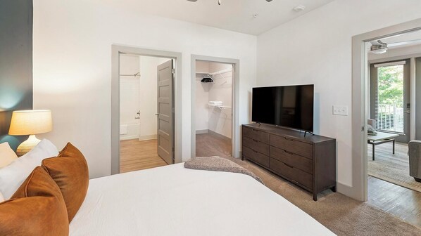 A hotel room with a bed, a dresser, a TV, and a bathroom visible through an open door. - Landing | Amazing 2BD, Gym, Yoga Studio (Charlotte)
