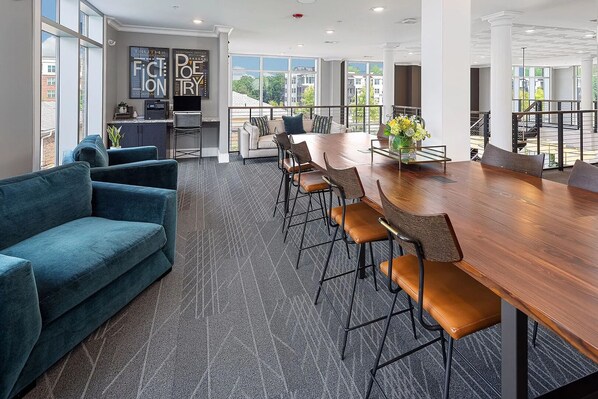 A modern conference room with a large wooden table, blue sofas, and a view of buildings through large windows.