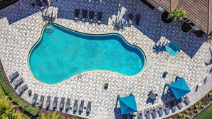 Vista aérea de una piscina rodeada de sillas de descanso y sombrillas, con un solárium de baldosas y palmeras.