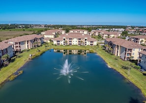 A residential complex with multiple apartment buildings, a central courtyard with a fountain, and a body of water.