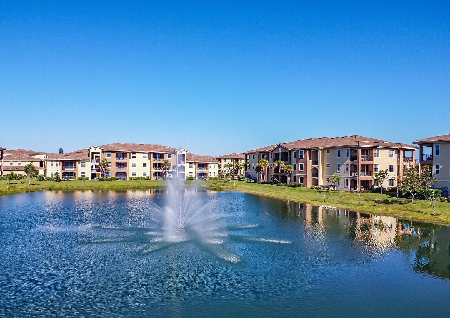 A residential area with a central fountain, multi-story buildings with balconies, and a clear blue sky.