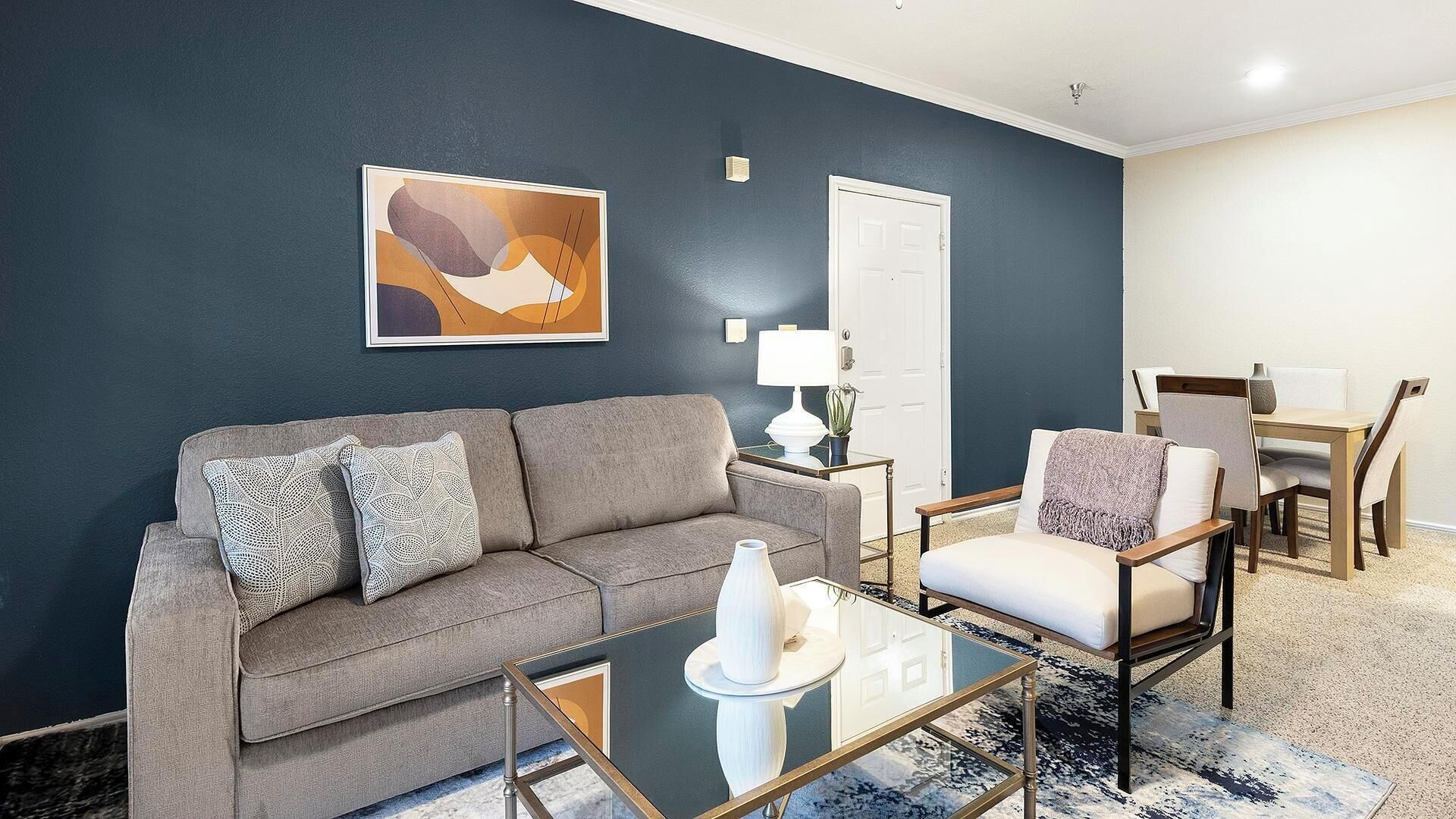 A living room with a grey sofa, a glass coffee table, and a chair.