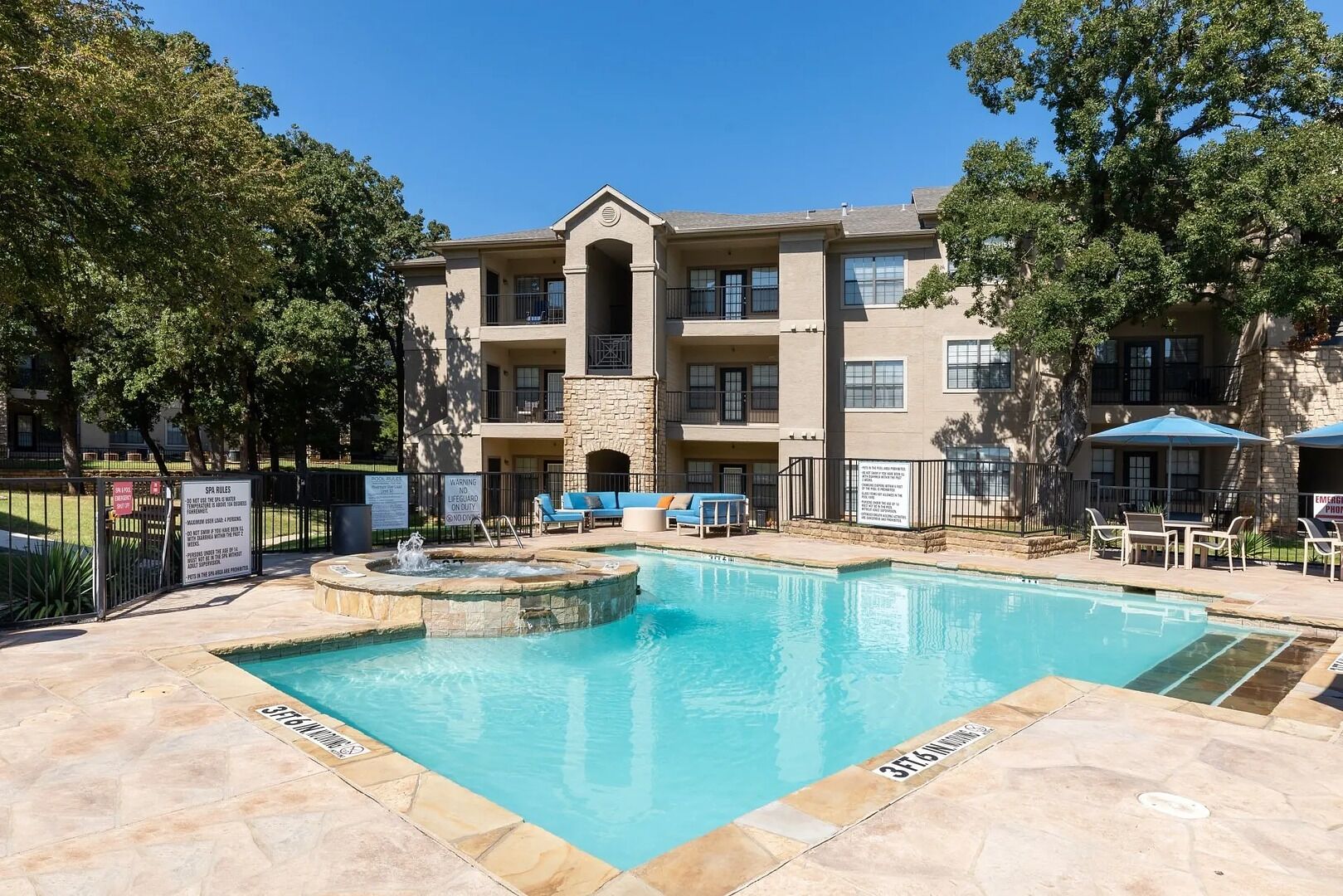 A pool area with a stone fountain, lounge chairs, and a building with multiple balconies.