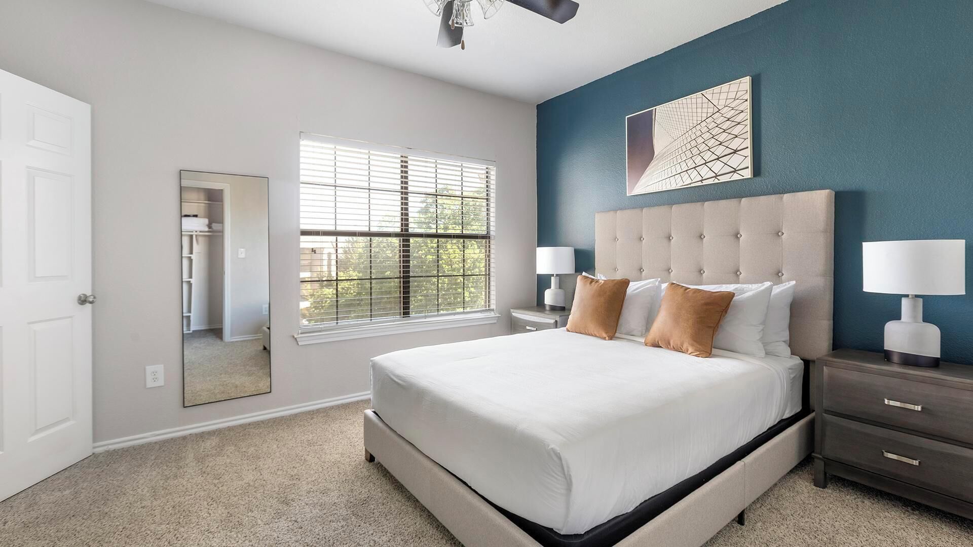 A bedroom with a large bed, bedside lamps, a window with blinds, and a wall-mounted artwork.