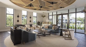 A spacious living room with a modern ceiling design, large windows offering a view of the outside, and a variety of seating arrangements.