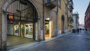 A cobblestone street with historic buildings, a shop with glass display windows, and a metal gate. - Charm and comfort at a stone's throw from the Arena (Verona)