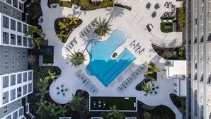 A rooftop pool surrounded by lounge chairs and palm trees, with modern buildings in the background. - Landing | Incredible 1BD, Pool, Gym (Cape Coral)