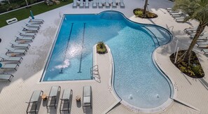 A large, rectangular swimming pool with a wavy edge, surrounded by lounge chairs and a tiled deck.