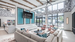 A modern hotel lobby with a large TV screen, comfortable seating, and large windows offering views of the outdoors. - Landing | Spectacular 1BD, Clubhouse, Pool (Cape Coral)