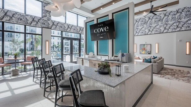 A modern kitchen with a large island, bar stools, and a TV screen displaying 'The Cove at 47th'. - Landing | Spectacular 1BD, Clubhouse, Pool (Cape Coral)