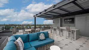 A rooftop terrace with a blue sofa, a dining area, and a bar. - Landing | Spectacular 1BD, Clubhouse, Pool (Cape Coral)