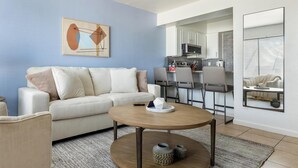 A modern living room with a sofa, a coffee table, and a kitchen in the background. - Landing | Beautiful 1BD in Maryvale Village (Phoenix)