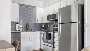 Una cocina compacta con armarios blancos, un refrigerador de acero inoxidable, un microondas y un horno empotrado.