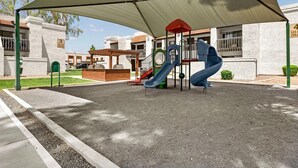Un parque infantil con zona de sombra, un tobogán y un conjunto de juegos.