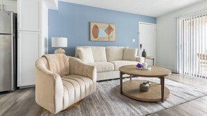 A modern living room with a beige sofa, a round coffee table, and a painting on the wall. - Landing | Chic 2BD in Maryvale Village (Phoenix)