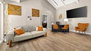 A modern living room with a sofa, two armchairs, a dining area, and a TV mounted on the wall. - Landing | Chic 2BD in Maryvale Village (Phoenix)