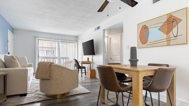 A modern living room with a sofa, a dining table with chairs, a TV, and a painting on the wall. - Landing | Chic 2BD in Maryvale Village (Phoenix)