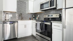 A modern kitchen with stainless steel appliances, white cabinetry, and a grey-tiled backsplash. - Landing | Chic 2BD in Maryvale Village (Phoenix)