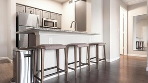 Una cucina moderna con elettrodomestici in acciaio inossidabile, un piano di lavoro in granito e tre sgabelli da bar.