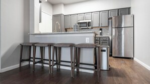 Una cocina moderna con gabinetes grises, electrodomésticos de acero inoxidable y una isla central con taburetes de bar.