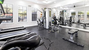 Un gimnasio con cintas de correr, máquinas de pesas y un espejo grande.