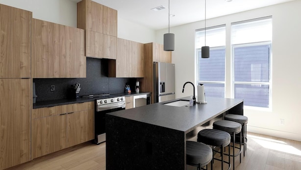 Una cocina moderna con armarios de madera, una isla central con taburetes de bar, un refrigerador de acero inoxidable y un ventanal que proporciona luz natural.