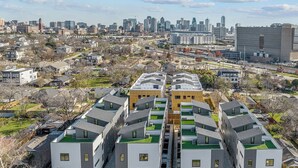 Ett modernt bostadskomplex med flera bostadshus, gröna tak och stadens silhuett som bakgrund.