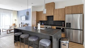 A modern kitchen with a central island, bar stools, stainless steel appliances, and wooden cabinetry. - Landing | Incredible 2BD in Downtown Dallas (Dallas)