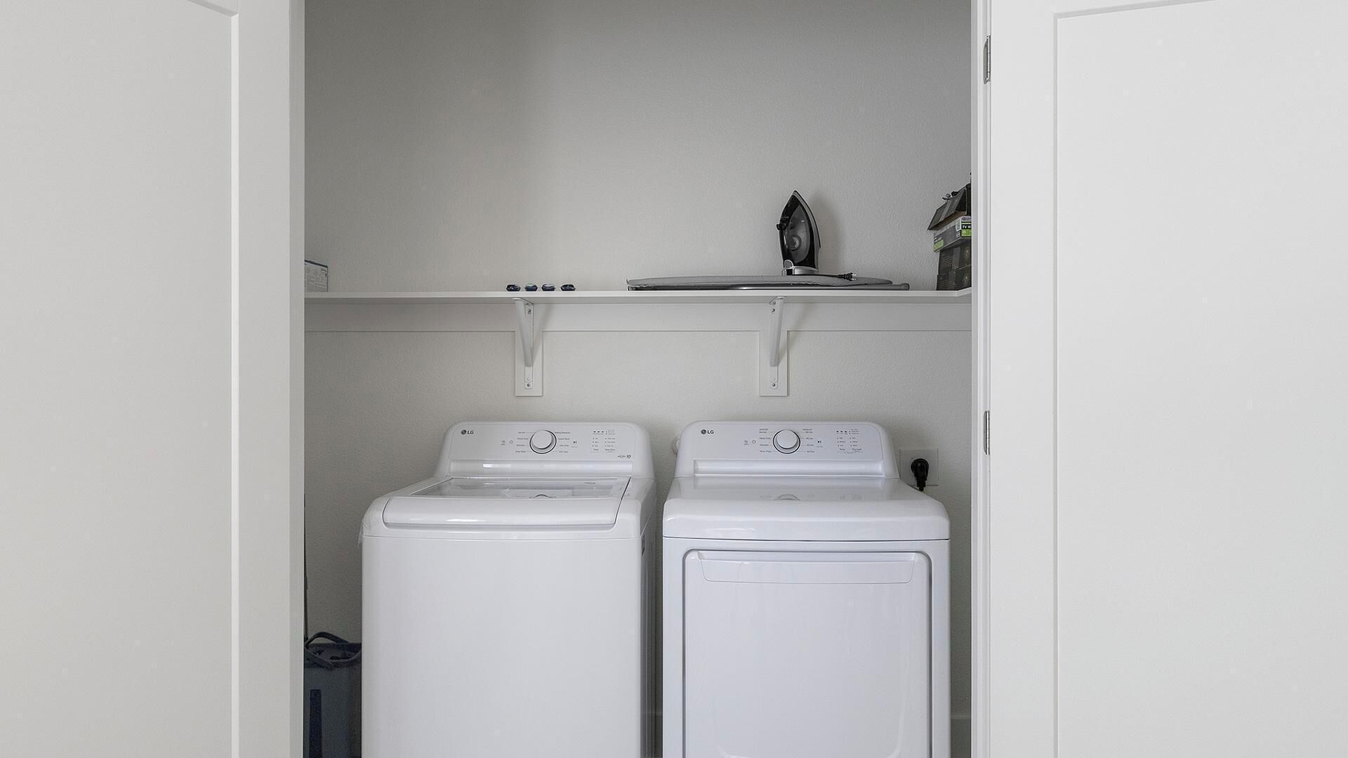 A laundry room with two white front-loading washing machines and a shelf above them.