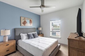 Ein Schlafzimmer mit einem Bett, Nachttischen, einem Deckenventilator, einem Fenster und einem Fernseher.