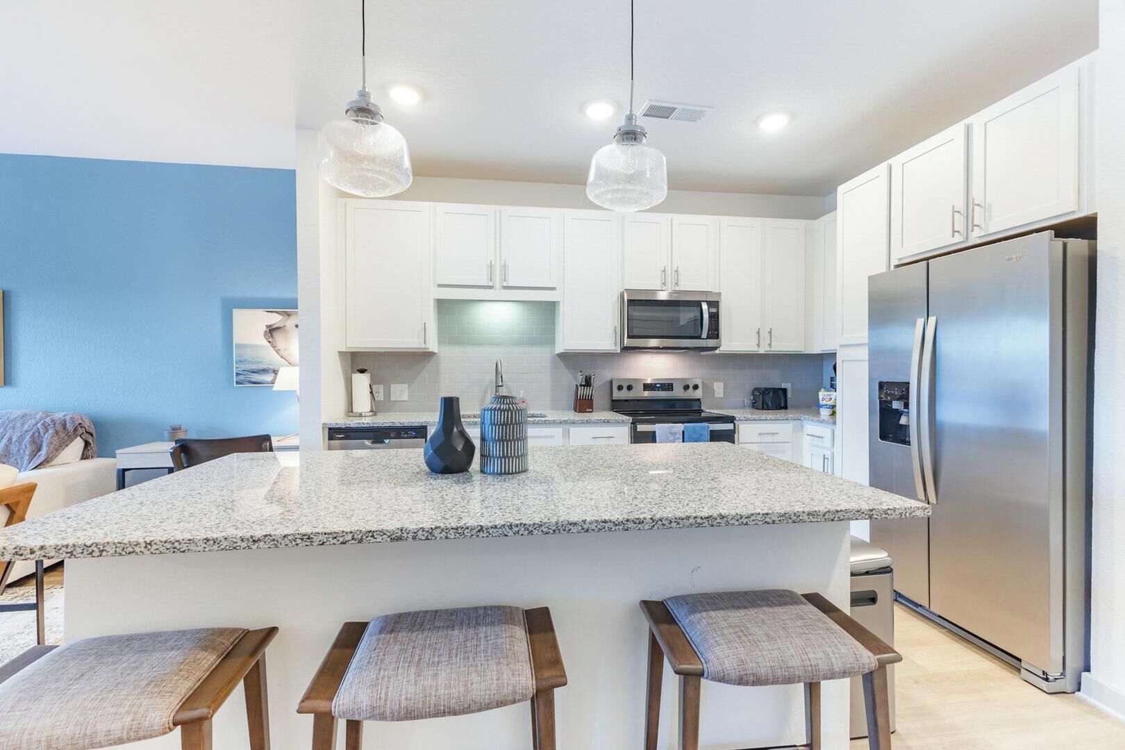 Une cuisine moderne avec des meubles blancs, un plan de travail en granit, des appareils électroménagers en acier inoxydable et des luminaires suspendus.