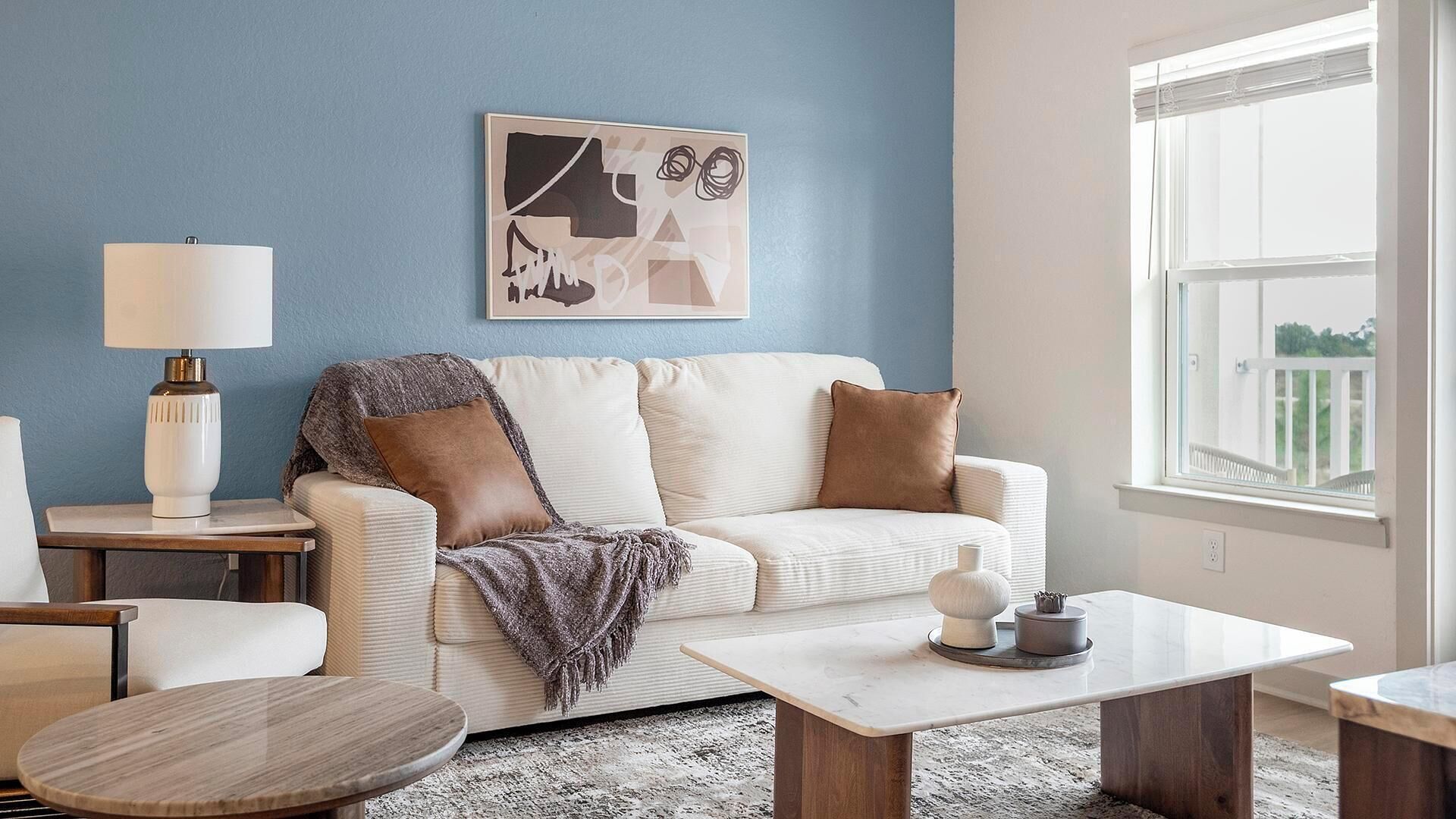 Una sala de estar con un sofá blanco, una mesa de centro, una lámpara y un cuadro en la pared.