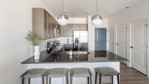Una cocina moderna con encimeras de granito, electrodomésticos de acero inoxidable y una isla central con taburetes de bar.
