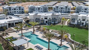 Un immeuble d’appartements moderne doté d’une piscine centrale, entouré de palmiers et de chaises longues.
