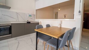A modern kitchen with a built-in oven, grey cabinets, and a wooden dining table with four grey chairs. - Cozy Apartment with Balcony in Xlendi Bay, Gozo (Munxar)